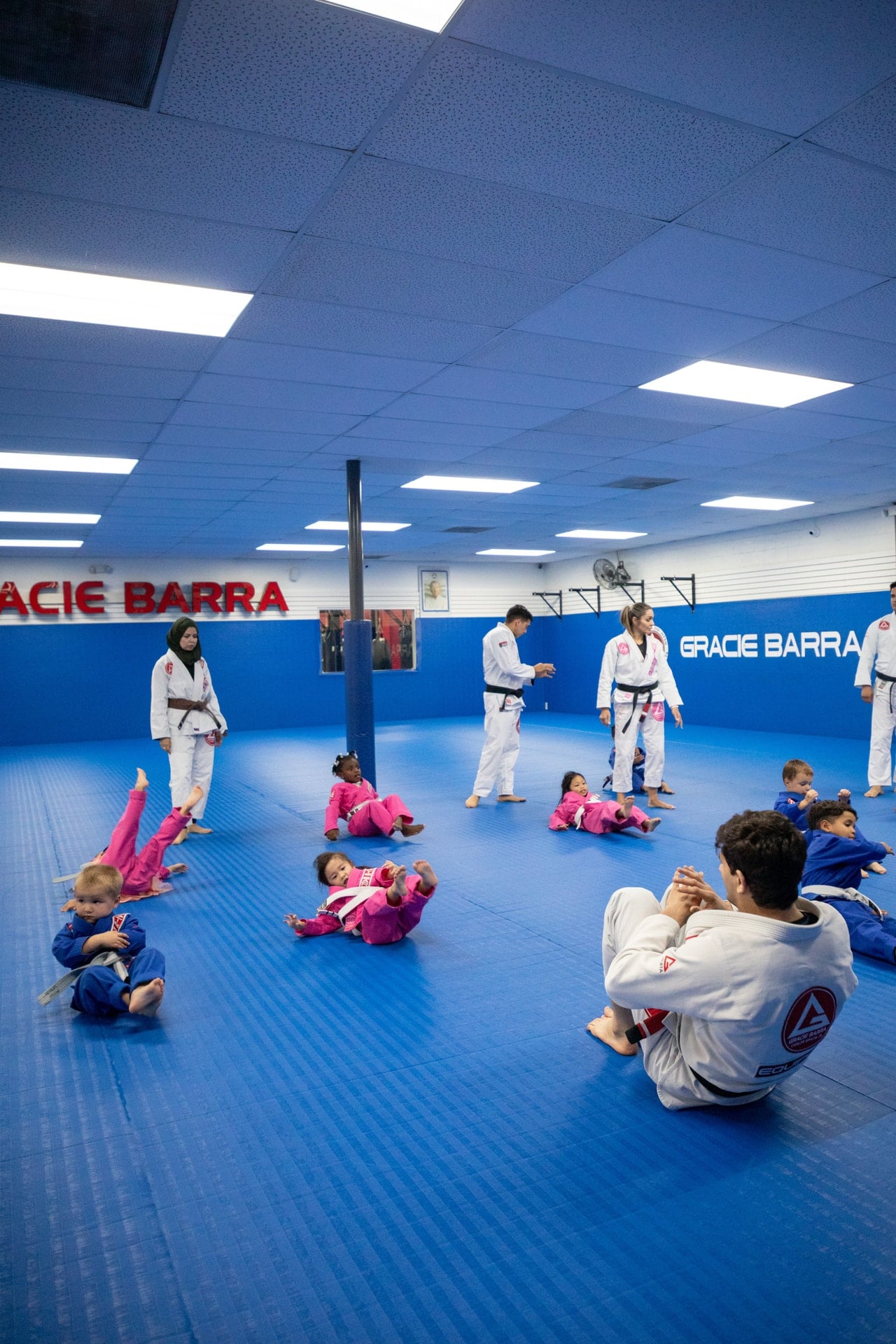 Young children in blue and pink gis practicing floor movements with instructors at Gracie Barra Westchase