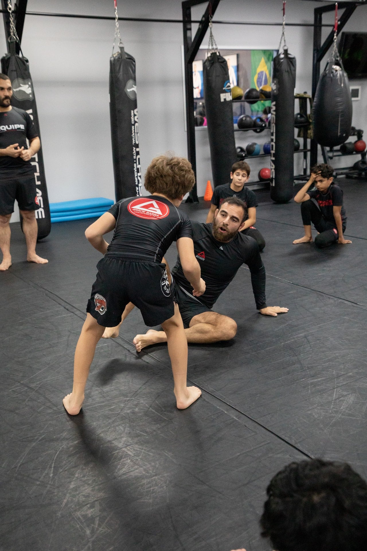 A Westchase instructor guiding a young student through a no-gi grappling drill as classmates watch