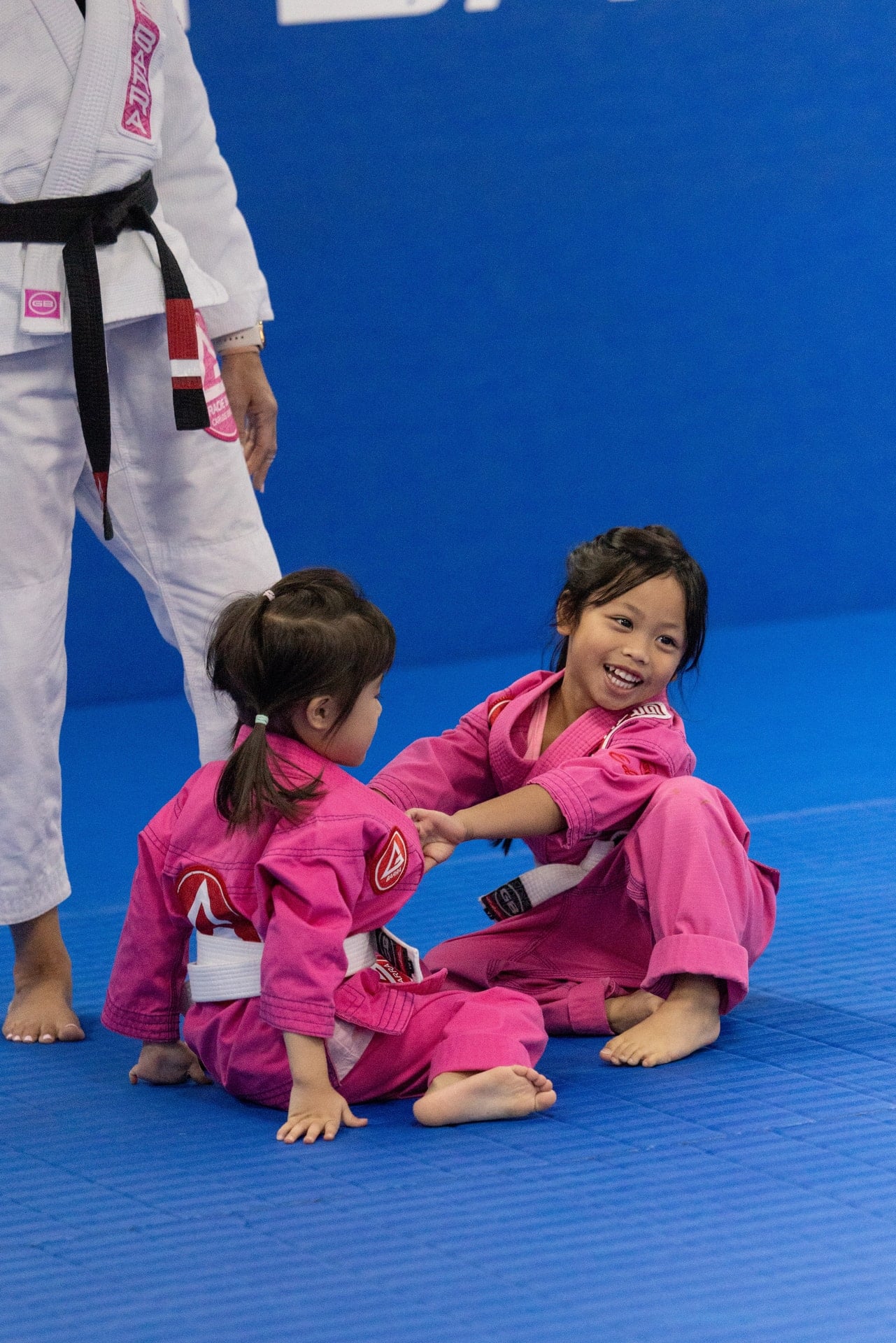 Two young Gracie Barra Westchase students in pink gis practicing together on the blue mats