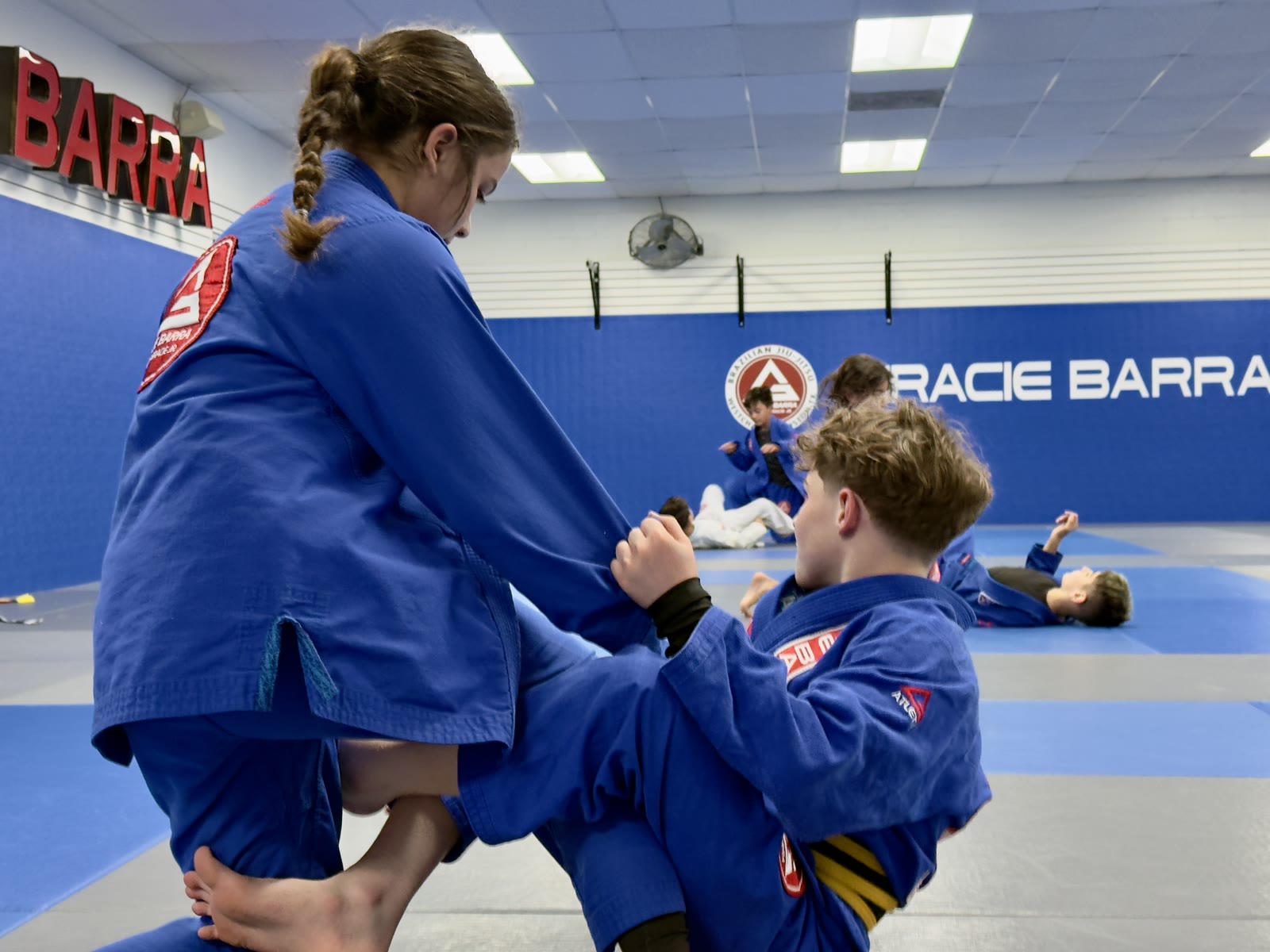 Kids Jiu-Jitsu Guard Practice – Gracie Barra Westchase Houston Two older kids in blue gis practicing guard and sleeve grips during Jiu-Jitsu class at Gracie Barra Westchase in Houston
