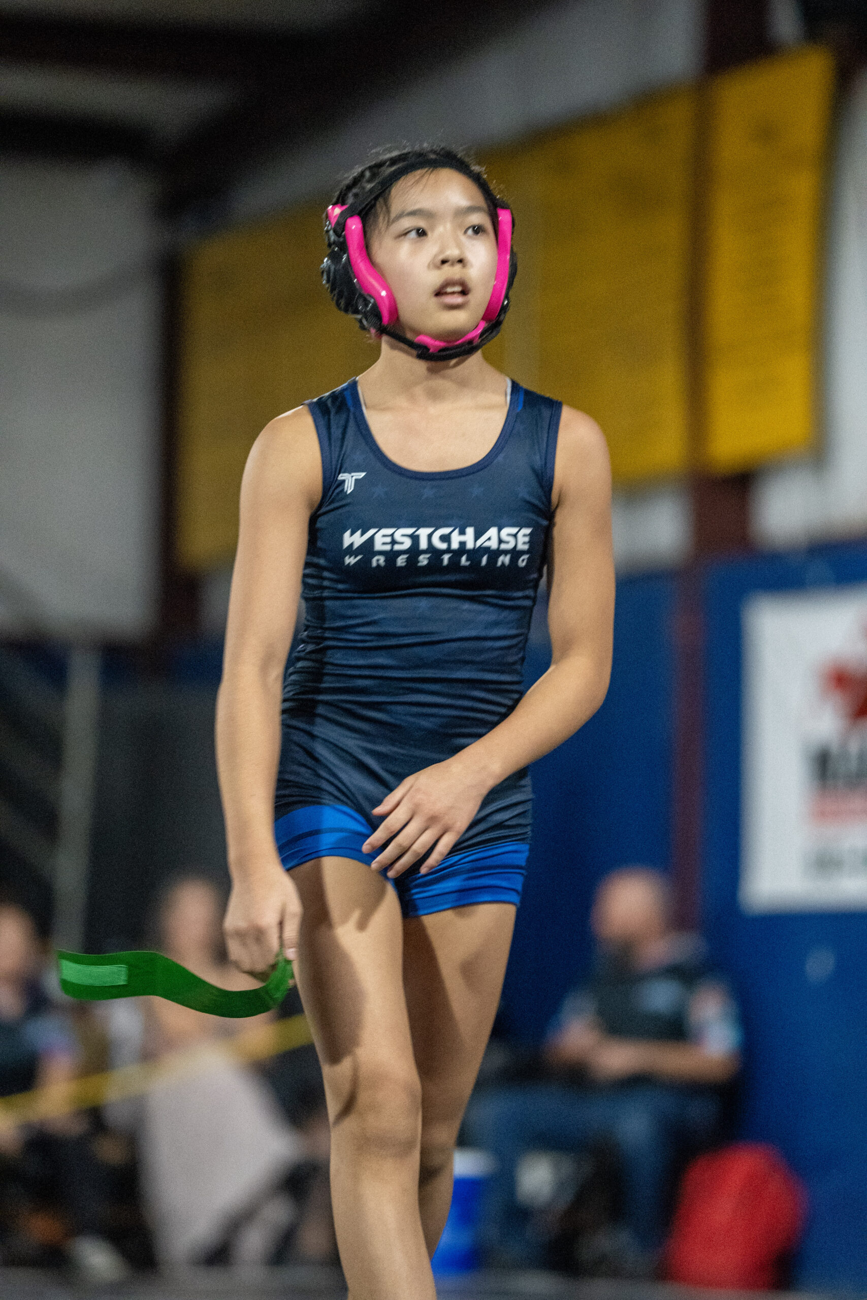 Young Westchase wrestler wearing a navy singlet and pink headgear on the competition mat.