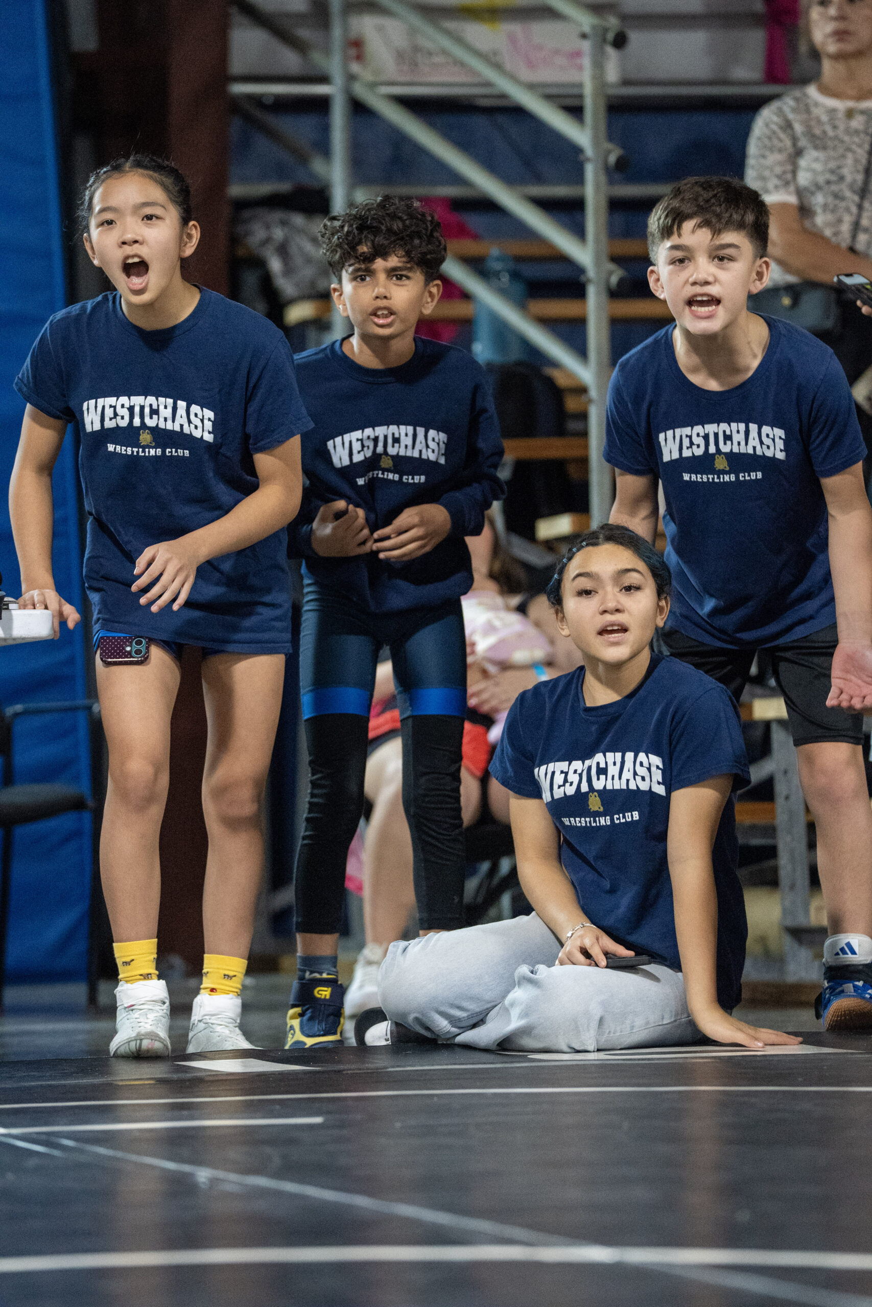 Young Westchase Wrestling teammates cheering beside the competition mat.